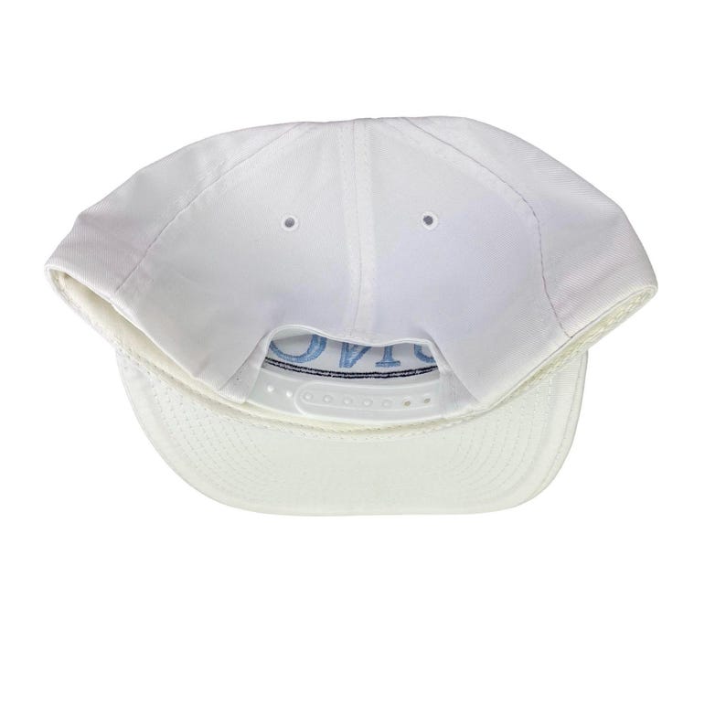 Puede incluir: Gorra de b&eacute;isbol blanca con visera curva y cierre trasero ajustable. La parte inferior de la visera es de un tono blanco m&aacute;s claro. La palabra "OVTA" est&aacute; bordada en azul claro en la parte trasera.