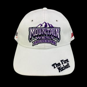 May include: White baseball cap with the text "MOUNTAIN WEST CONFERENCE" in purple and gray embroidery. The phrase "The First Kickoff" is embroidered on the brim. The cap has a curved brim and a structured crown.