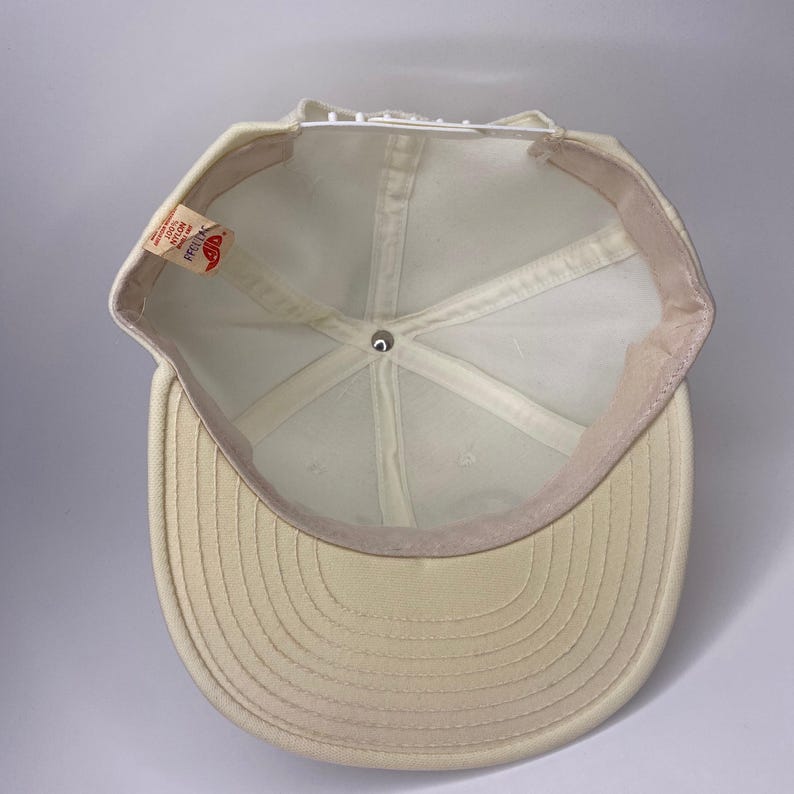 K&ouml;nnte beinhalten: Cremefarbene Baseballkappe mit gebogenem Schirm. Die Innenseite hat eine wei&szlig;e Krone und ein Schwei&szlig;band. Ein kleines Etikett ist an der Seite sichtbar. Die Kappe ist aus weichem, strukturiertem Material.