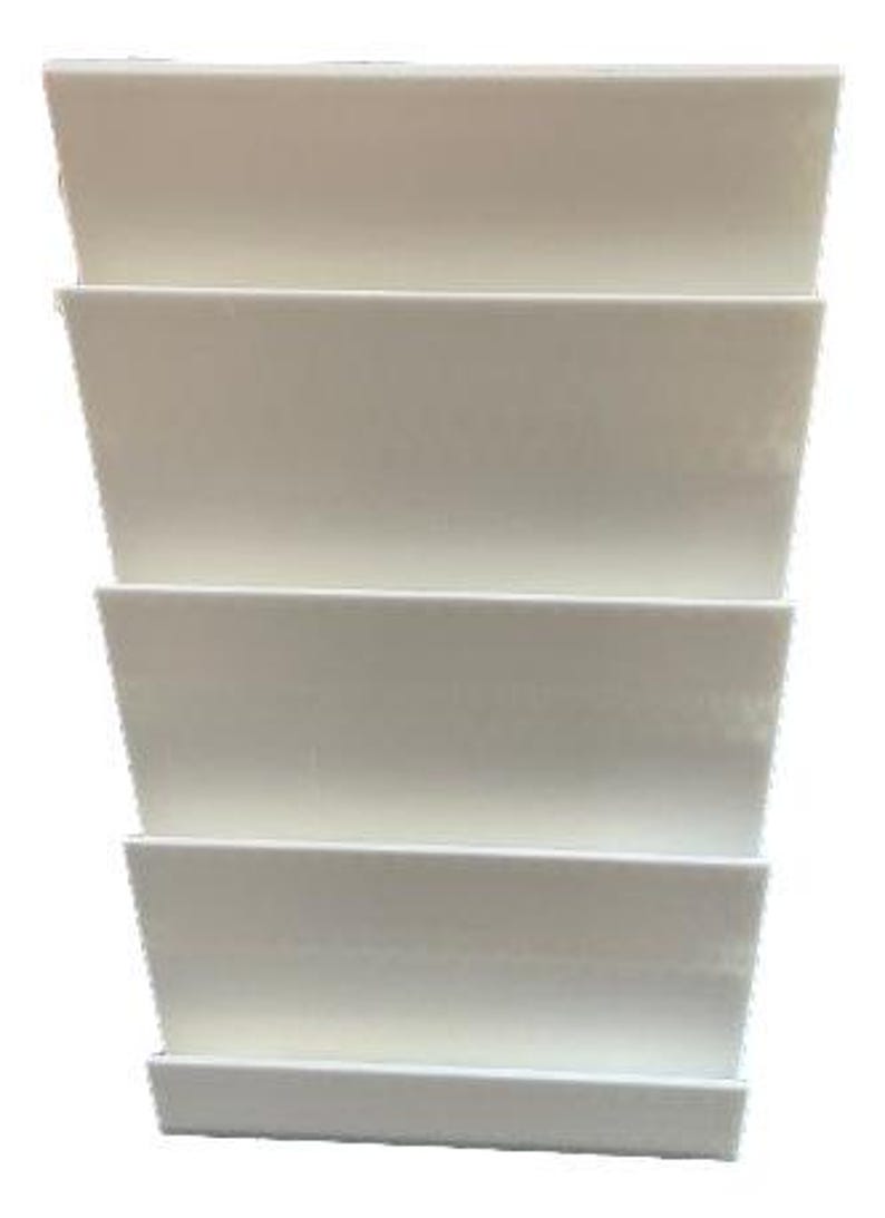 May include: A stack of four off-white, rectangular, tiered shelves. Each shelf is slightly angled, creating a stepped appearance. The shelves are made of a solid material and are suitable for displaying items.