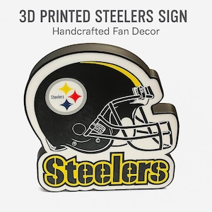 Puede incluir: Un letrero de los Steelers impreso en 3D con forma de casco de fútbol. El letrero es negro, blanco y amarillo, con el logotipo de los Steelers. El texto "3D PRINTED STEELERS SIGN Handcrafted Fan Decor" está en la parte superior y "Steelers" en la parte inferior.