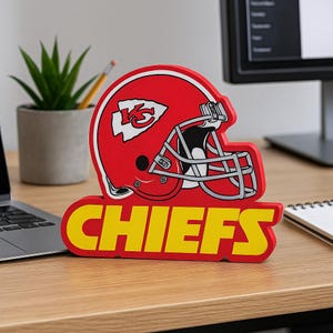 May include: A red and white Kansas City Chiefs helmet-shaped desk ornament. The word "CHIEFS" is displayed in yellow block letters below the helmet. The ornament is on a wooden desk.