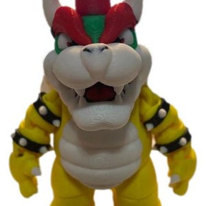 May include: A 3D-printed Bowser figurine, featuring a yellow body, white belly, and a red and green spiky crown. The figure has white horns, black studded armbands, and an open mouth revealing red. A collectible item.