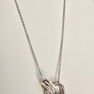 May include: A silver-coloured necklace featuring a pendant composed of three interlocking, textured circular rings. The pendant is suspended from a delicate, thin silver-coloured chain that connects to the top of the circular ring cluster.