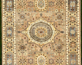 May include: A rectangular area rug featuring a tan background with a central medallion and repeating floral motifs in shades of blue, cream, and brown. The rug has a wide border with intricate geometric patterns and symmetrical floral designs.