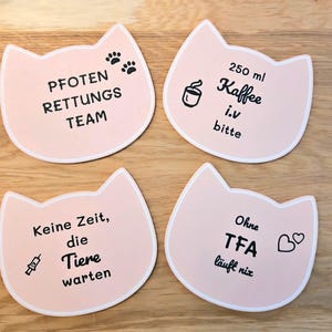 Könnte beinhalten: Vier rosa katzenförmige Untersetzer mit weißen Rändern. Jeder Untersetzer hat schwarzen Text und Grafiken. Einer sagt "PFOTEN RETTUNGS TEAM" mit Pfotenabdrücken. Ein anderer sagt "250 ml Kaffee i.v bitte" mit einer Kaffeetasse. Der dritte sagt "Keine Zeit, die Tiere warten".