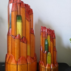 Puede incluir: Dos esculturas abstractas y geométricas. La más grande mide aproximadamente 30 cm de altura, y la más pequeña, unos 15 cm. Son principalmente naranjas con detalles rojos y amarillos, y contornos negros. El diseño se asemeja a un paisaje urbano o una cordillera estilizada.