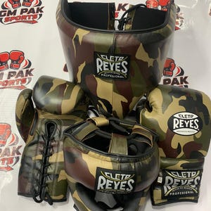 May include: A set of boxing gear in a camouflage pattern. The set includes a head guard, boxing gloves, and hand wraps. The gloves and headgear feature the "CLETO REYES" logo. The gear is designed for professional boxing training and competition.