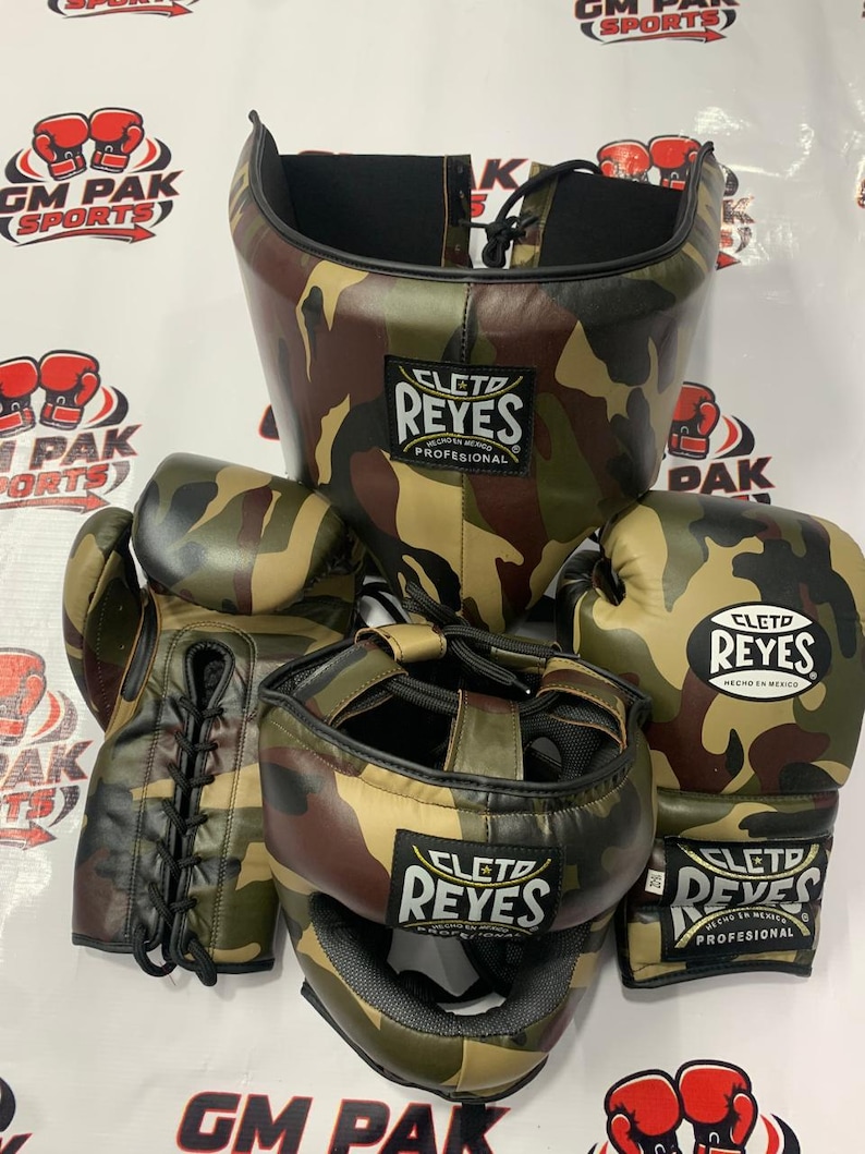 May include: A set of boxing gear in a camouflage pattern. The set includes a head guard, boxing gloves, and hand wraps. The gloves and headgear feature the "CLETO REYES" logo. The gear is designed for professional boxing training and competition.