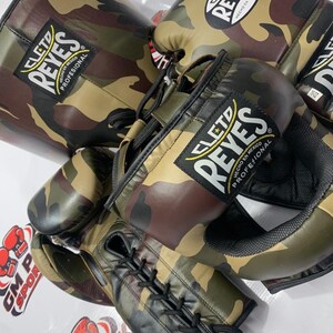 May include: Camouflage boxing gloves and a matching head guard. The gloves and headgear feature a green, brown, and black camouflage pattern. The brand name "CLETO REYES" is visible on the gloves and headgear.