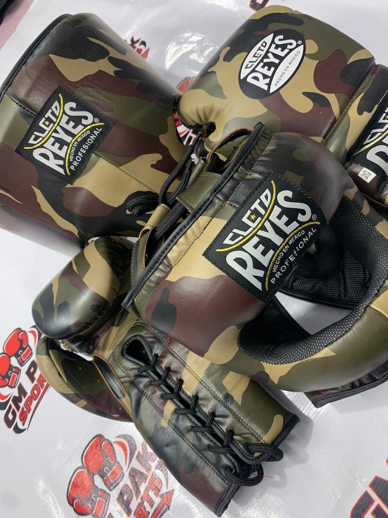 May include: Camouflage boxing gloves and a matching head guard. The gloves and headgear feature a green, brown, and black camouflage pattern. The brand name "CLETO REYES" is visible on the gloves and headgear.