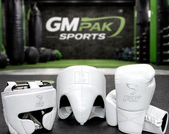 May include: White boxing headgear, gloves, and head protector set. The gloves and headgear feature the "FLY" logo. The background includes the text "GM PAK SPORTS". The set is designed for boxing and martial arts training.