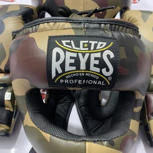 May include: Camouflage boxing headgear and gloves set. The headgear features the "CLETO REYES" logo and the text "HECHO EN MEXICO PROFESIONAL". The set is in shades of brown, green, and black.
