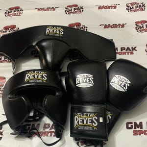 Peut inclure: Un ensemble d'équipement de boxe noir Cleto Reyes comprenant une coquille, un casque et une paire de gants de boxe. Chaque article présente l'écusson logo Cleto Reyes blanc et jaune avec le texte Profesional Hecho en Mexico.