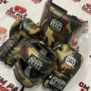 May include: A collection of camouflage boxing gear, including gloves, headgear, and a face protector. The gear features the "CLETO REYES" logo. The color scheme includes shades of green, brown, and tan.