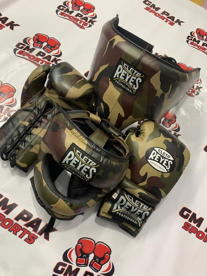 May include: A set of Cleto Reyes boxing gear in a camouflage pattern. The set includes boxing gloves, a head guard, and a face protector. The gloves and headgear feature the Cleto Reyes logo. The background has the text "GM PAK SPORTS".