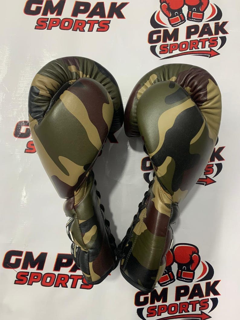 May include: Pair of camouflage boxing gloves. The gloves feature a green, brown, and tan pattern. The text "GM PAK SPORTS" is visible in the background.