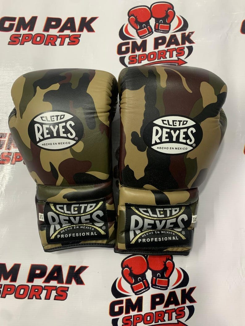 May include: Pair of camouflage boxing gloves with the "CLETO REYES" logo. The gloves are in shades of green, brown, and black. The text "HECHO EN MEXICO" is also visible. The gloves are labeled "PROFESIONAL".