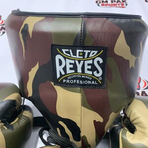 May include: Camouflage-patterned boxing headgear and gloves. The headgear features a black trim and a label that reads "CLETO REYES HECHO EN MEXICO PROFESIONAL". The gloves and headgear have a brown, green, and tan camouflage design.