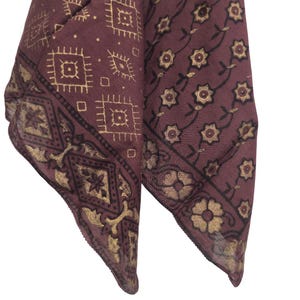 Può includere: Due sciarpe bordeaux con motivi oro e neri. Una presenta forme geometriche, l'altra un design floreale. Le sciarpe sono piegate, mostrando gli intricati dettagli del tessuto.