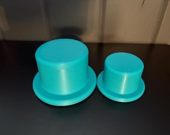 May include: Two turquoise top hats, one larger than the other, are displayed on a dark surface. The hats have a classic top hat shape with a cylindrical crown and a wide brim. The hats are made of a solid material.