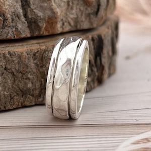 Peut inclure: Une bague en argent avec une surface texturée et un design de bande. La bague est présentée sur une surface en bois avec une esthétique naturelle et rustique. C'est un bijou.