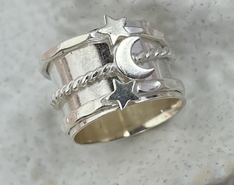 May include: A silver ring with a celestial design. The ring features a crescent moon and star accents, with a twisted rope detail. The ring is made of a shiny, metallic material.