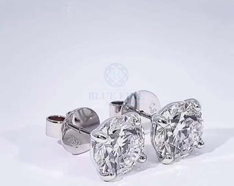 May include: A pair of diamond stud earrings. Each earring features a round, brilliant-cut diamond set in a silver or white gold setting. The earrings are displayed on a white surface with soft lighting.