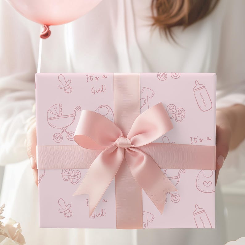 K&ouml;nnte beinhalten: Eine rosa Geschenkbox mit Baby-Illustrationen und dem Text "It's a Girl!". Die Box ist mit einem gro&szlig;en rosa Satinband und einer Schleife gebunden, ideal f&uuml;r eine Babyparty oder zur Geburt.