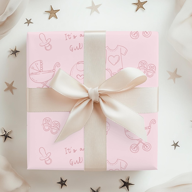 K&ouml;nnte beinhalten: Eine rosa Geschenkbox mit Baby-Motiven und dem Text "It's a Girl!". Sie ist mit einem cremefarbenen Band und einer Schleife gebunden. Verziert mit sternf&ouml;rmigen Dekorationen, ideal f&uuml;r Babys.
