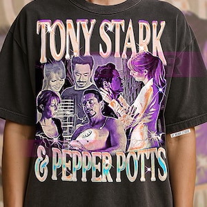 May include: Dark gray t-shirt featuring a vintage-style graphic of Tony Stark and Pepper Potts with the text "TONY STARK & PEPPER POTTS". The design includes images of the characters in a distressed, faded style.