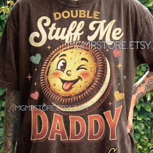 May include: Brown t-shirt with a graphic of a winking cookie with the words "DOUBLE Stuff Me DADDY". The shirt also has the text "MGMSTORE.ETSY.COM" and "Espresso comfort colors".