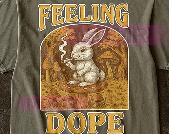 May include: Olive green t-shirt with a graphic of a rabbit smoking a cigarette while sitting on a mushroom. The text "FEELING DOPE" is arched above and below the illustration in a yellow font.