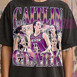 Pode incluir: Camiseta cinza escuro com um gráfico de Caitlin Clark em um uniforme roxo do Fever. O design inclui o nome "CAITLIN CLARK" em uma fonte roxa e branca, com várias imagens da jogadora de basquete.