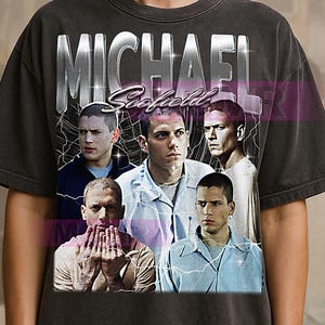 Op de afbeelding: Donkergrijze t-shirt met een afbeelding van Michael Scofield uit de tv-serie Prison Break. Het ontwerp bevat meerdere afbeeldingen van het personage met de naam "MICHAEL Scofield" in een zilveren, verweerde lettertype.