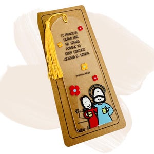 May include: A clear acrylic bookmark with a yellow tassel, featuring the text "TU PRINCESA, SIRVA MIA, NO TEMAS PORQUE YO ESTOY CONTIGO -AFIRMA EL SENOR-" and "Jeremias 46:28". The bookmark has colorful flower accents and a cartoon illustration of two figures.