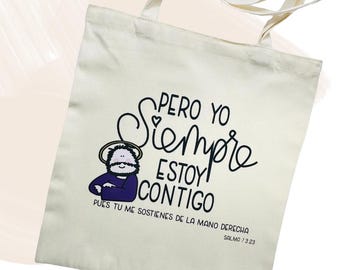 May include: Cream tote bag featuring black script and a cartoon illustration. The text reads "PERO YO SIEMPRE ESTOY CONTIGO" with a Bible verse reference. The illustration depicts a figure with a halo.