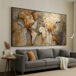 May include: A large framed artwork of a 3D world map, with a textured, stone-like finish in shades of brown, beige, and grey. The map is displayed above a grey sofa with orange and white cushions, creating a modern living space.