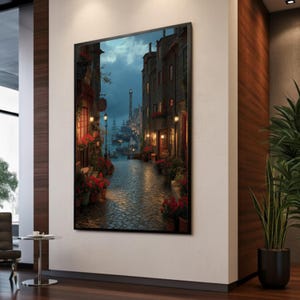 May include: A framed print shows a European street scene at dusk. Buildings with warm lights line the cobblestone street. Red flowers in pots decorate the street, leading to a distant lighthouse and ships under a cloudy sky.