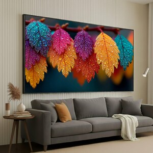 May include: A large framed canvas print depicting vibrant leaves with water droplets. The leaves transition from teal to pink, purple, and orange. The artwork hangs above a grey sofa in a living room setting.