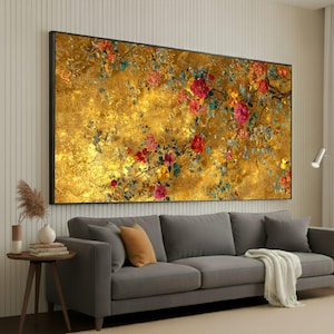 Puede incluir: Obra de arte enmarcada de gran tamaño con un fondo dorado texturizado. La obra presenta un diseño floral con flores rojas, rosas y amarillas, y hojas verdes y azules. La obra se exhibe sobre un sofá gris.