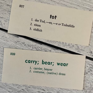 May include: Two vintage flashcards with German and English vocabulary words. The top card reads "tot" with German translations. The bottom card reads "carry; bear; wear" with English translations. The cards are cream-colored with black and green text.