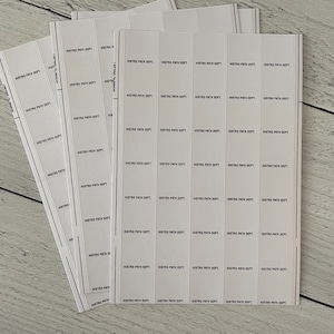 Puede incluir: Una pila de etiquetas rectangulares blancas con el texto "HISTRO PATH DEPT." impreso en negro. Las etiquetas están dispuestas en filas y columnas, con algunas etiquetas en tiras verticales. El fondo es un veteado de madera clara.