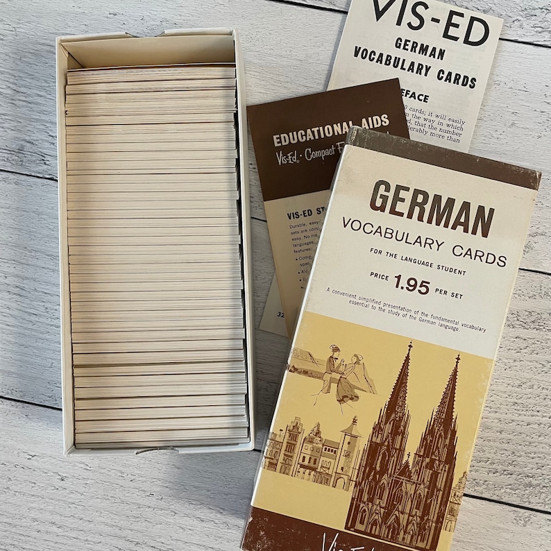 May include: A set of vintage German vocabulary cards in a box. The box and cards are beige and white. The box has the words "GERMAN VOCABULARY CARDS" printed on it, along with an illustration of a cathedral and people. The price is $1.95 per set.