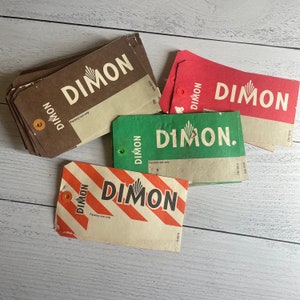May include: A collection of vintage DIMON tags in various colors, including brown, red, green, and cream with orange diagonal stripes. Each tag features the DIMON logo and text, with a hole for attachment. The tags are arranged on a light wood surface.