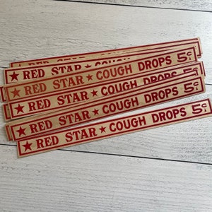 May include: Several vintage Red Star Cough Drops signs. Each sign is rectangular with red text and a star design. The text reads "RED STAR COUGH DROPS 5¢" on a beige background.