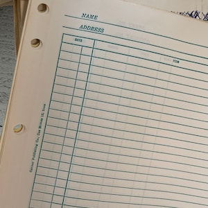 May include: Close-up of a vintage ledger paper with green ruled lines and pre-printed fields for Name, Address, Date, and Item. The paper has three hole punches and text that reads "Garner Publishing Co., Des Moines 13, Iowa."
