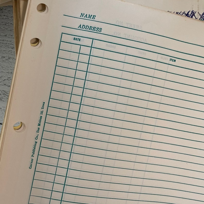 May include: Close-up of a vintage ledger paper with green ruled lines and pre-printed fields for Name, Address, Date, and Item. The paper has three hole punches and text that reads "Garner Publishing Co., Des Moines 13, Iowa."