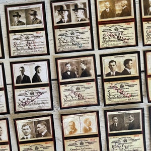Op de afbeelding: Een verzameling vintage kaarten met sepiafoto's van mannen in pakken en hoeden. Elke kaart bevat tekst, handtekeningen en nummers, met een donkere rand en een cr&egrave;mekleurige achtergrond. De kaarten zijn gerangschikt op een licht oppervlak.