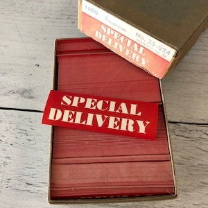 May include: A box of red Dennison Special Delivery labels. The labels are rectangular with the words "SPECIAL DELIVERY" printed in white. The box is brown with the text "Dennison" and "No. 35-024" printed on it.